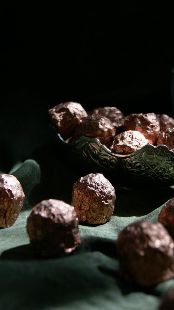 Luxurious dark chocolate truffles elegantly wrapped in foil, presented in a decorative bowl.
