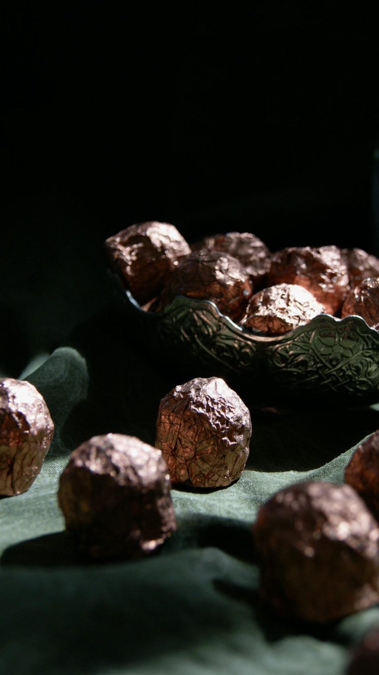 Luxurious dark chocolate truffles elegantly wrapped in foil, presented in a decorative bowl.