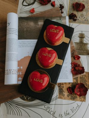 Red heart desserts with 'love' inscriptions on slate, surrounded by papers and petals.