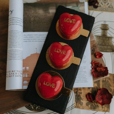 Red heart desserts with 'love' inscriptions on slate, surrounded by papers and petals.